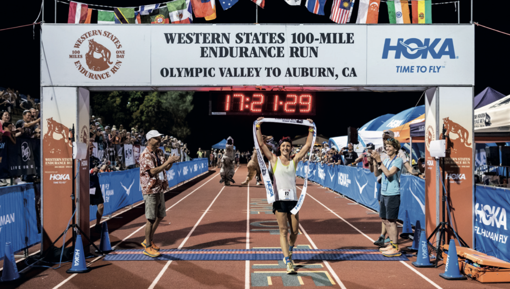 A photo of a man at the finish line holding the finish tape in the air